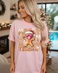 Woman wearing a pink 'Merry Christmas' t-shirt with a gingerbread man graphic in a festive living room. Christmas shirts Australia