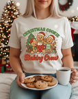 Person wearing a 'Christmas Cookie Baking Crew' t-shirt, holding cookies and a mug in a festive setting. Christmas t shirts Australia